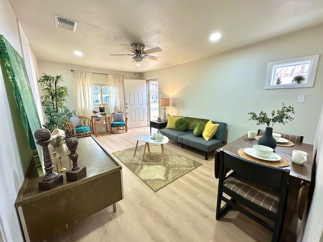 living room with recessed lighting, visible vents, light wood-style flooring, ceiling fan, and a textured ceiling