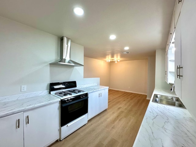 kitchen featuring range with gas stovetop, white cabinetry, a sink, and wall chimney range hood