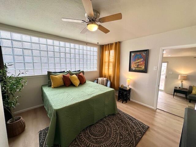 bedroom with baseboards, ceiling fan, light wood-style flooring, and a textured ceiling