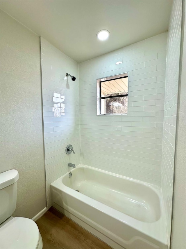 bathroom featuring baseboards, a textured wall, toilet, wood finished floors, and shower / washtub combination