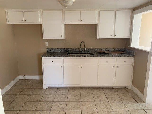 kitchen with white cabinetry, sink, dark stone counters, and light tile patterned flooring