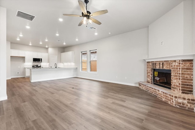 unfurnished living room featuring ceiling fan, sink, a brick fireplace, and light wood-type flooring