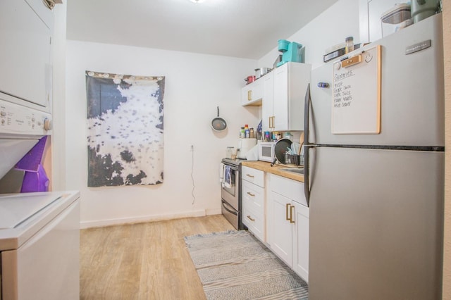 kitchen featuring light wood-type flooring, stacked washer and clothes dryer, white cabinets, and appliances with stainless steel finishes