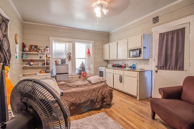 bedroom with ceiling fan, sink, wooden walls, and light hardwood / wood-style floors