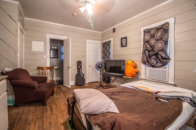 bedroom featuring connected bathroom, wood-type flooring, ceiling fan, and wood walls