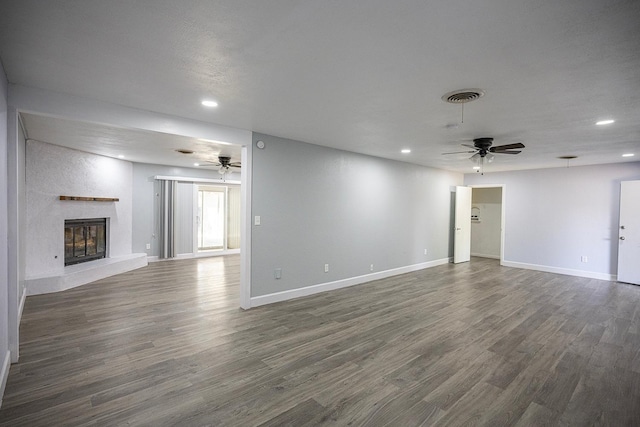 unfurnished living room with ceiling fan, a large fireplace, and dark hardwood / wood-style flooring