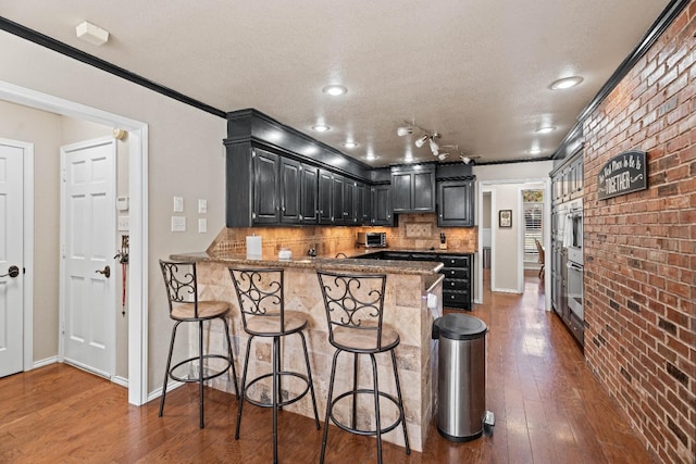 kitchen with dark hardwood / wood-style flooring, backsplash, kitchen peninsula, and a kitchen bar