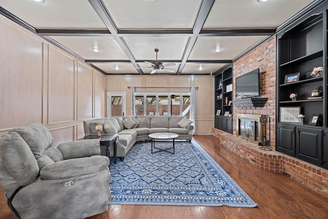 living room featuring hardwood / wood-style floors, built in features, coffered ceiling, ceiling fan, and a brick fireplace