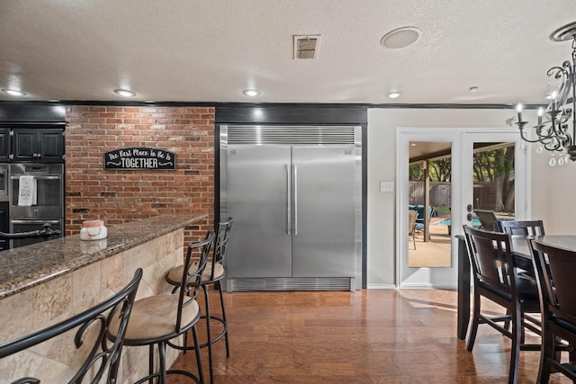 kitchen with appliances with stainless steel finishes, dark stone countertops, a textured ceiling, and dark hardwood / wood-style flooring