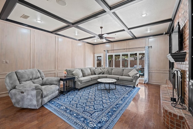 living room featuring ceiling fan, dark hardwood / wood-style flooring, coffered ceiling, and a fireplace