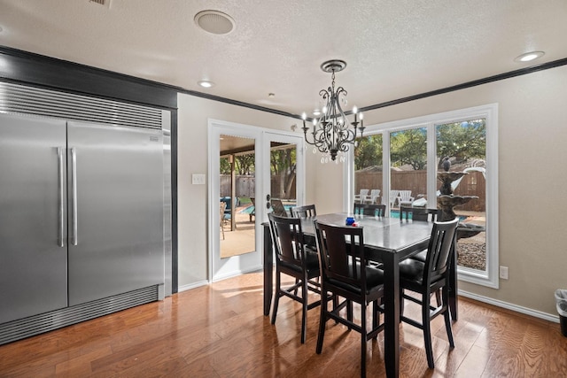 dining room featuring hardwood / wood-style flooring, ornamental molding, a textured ceiling, and a notable chandelier