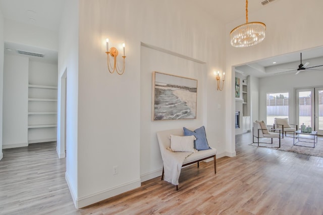 sitting room featuring ceiling fan with notable chandelier, light hardwood / wood-style floors, and built in features