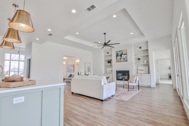 living room with built in features, light hardwood / wood-style floors, and a tray ceiling