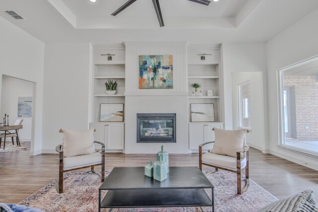 living room with a raised ceiling, built in features, and light hardwood / wood-style flooring