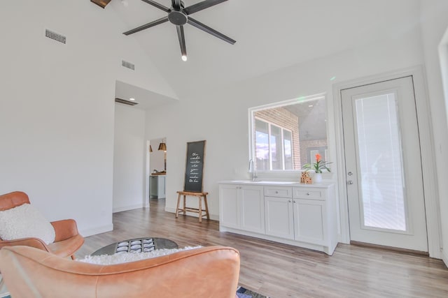 living room with ceiling fan, high vaulted ceiling, sink, and light wood-type flooring