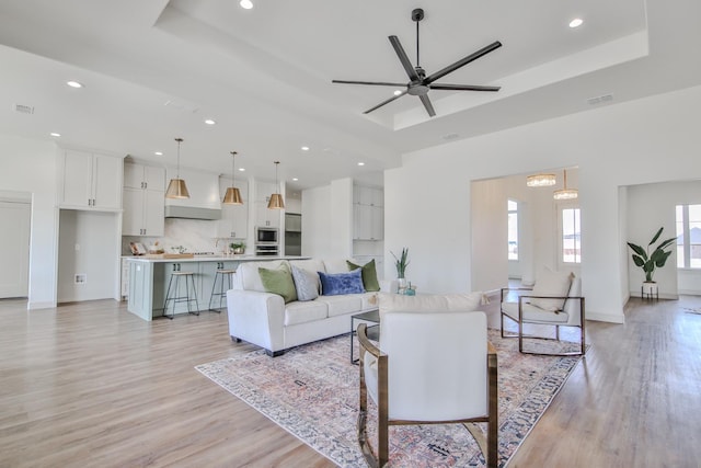 living room featuring ceiling fan, a raised ceiling, and light hardwood / wood-style floors