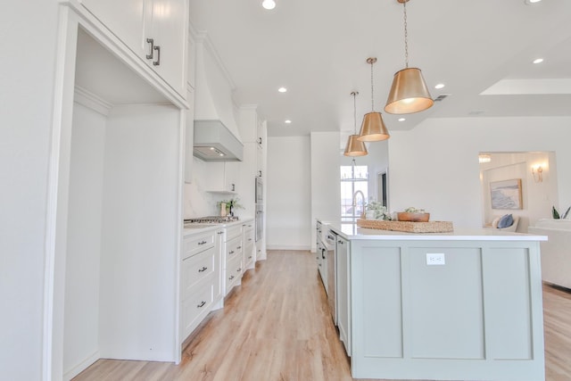 kitchen with premium range hood, an island with sink, white cabinets, hanging light fixtures, and light hardwood / wood-style floors