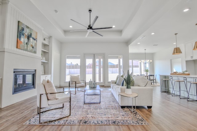 living room featuring ceiling fan with notable chandelier, built in features, and light hardwood / wood-style flooring