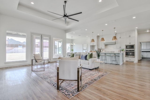 living room featuring a tray ceiling, light hardwood / wood-style floors, and ceiling fan with notable chandelier