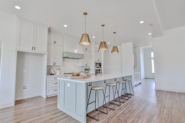 kitchen with white cabinetry, an island with sink, a breakfast bar area, hanging light fixtures, and light hardwood / wood-style floors