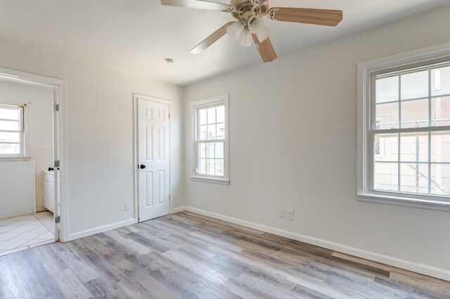 unfurnished bedroom featuring a closet, ensuite bath, multiple windows, and light hardwood / wood-style flooring