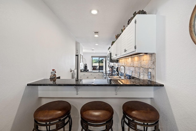 kitchen featuring white cabinetry, a breakfast bar, kitchen peninsula, and sink