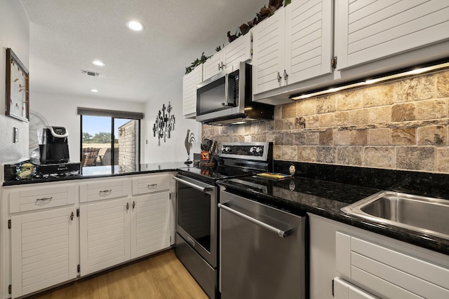 kitchen featuring appliances with stainless steel finishes, white cabinets, backsplash, dark stone counters, and light hardwood / wood-style flooring