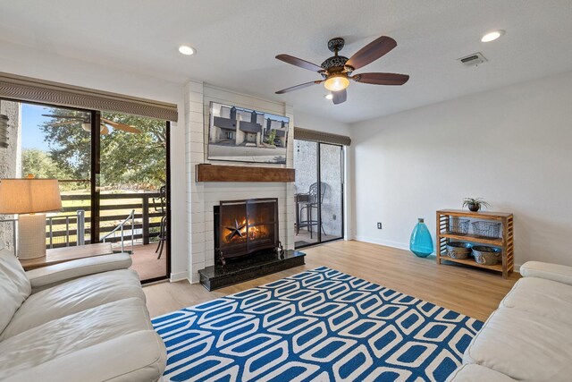 living room featuring a fireplace, ceiling fan, and light wood-type flooring