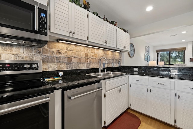 kitchen featuring sink, white cabinetry, dark stone countertops, appliances with stainless steel finishes, and backsplash