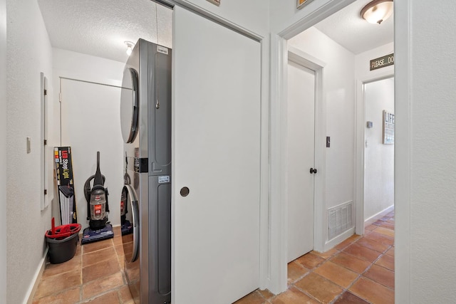 hall with a textured ceiling and stacked washer / dryer