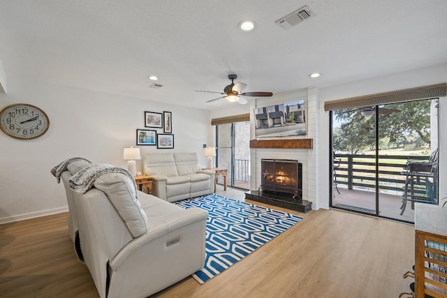 living room with ceiling fan, hardwood / wood-style floors, a brick fireplace, and a textured ceiling