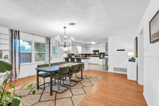 2509 61st St, Lubbock, TX 79413 - dining room featuring a chandelier, light wood-type flooring, plenty of natural light, a textured ceiling, and wainscoting