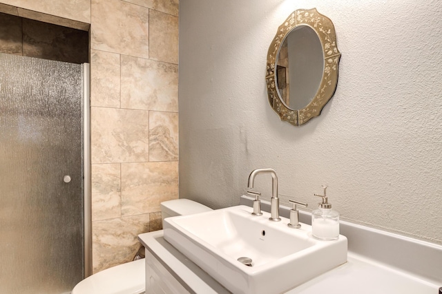 bathroom with an enclosed shower, toilet, a textured wall, and a sink