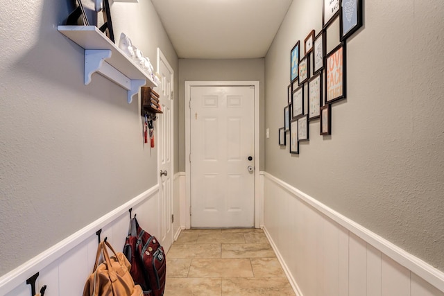 doorway to outside with a textured wall, wainscoting, and a decorative wall