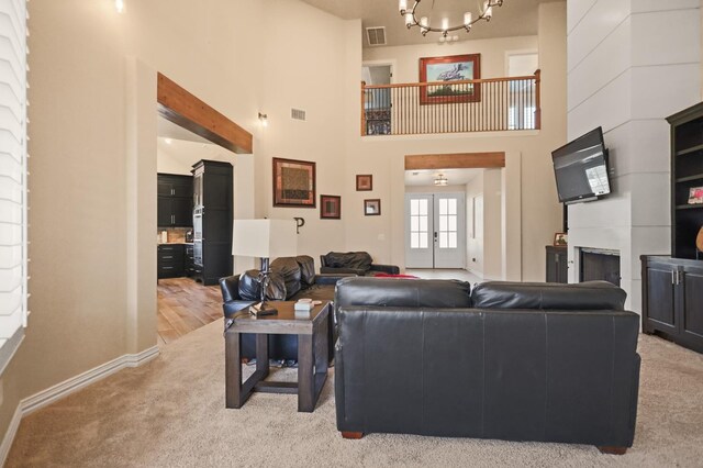 living room with light carpet, a towering ceiling, french doors, and an inviting chandelier