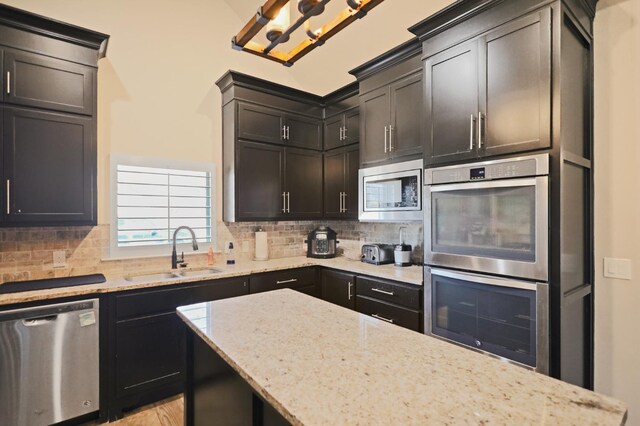 kitchen featuring tasteful backsplash, sink, light stone counters, and appliances with stainless steel finishes