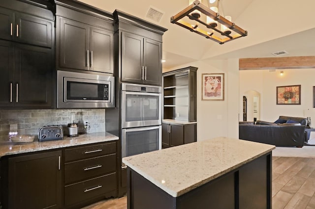 kitchen featuring backsplash, stainless steel appliances, light stone countertops, and a kitchen island