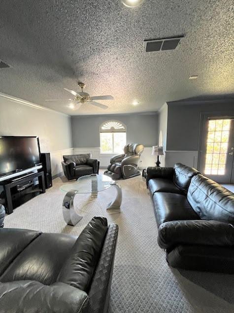 carpeted living room featuring crown molding, ceiling fan, and a textured ceiling