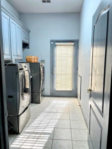 laundry room with light tile patterned floors, a textured ceiling, cabinets, and washing machine and clothes dryer