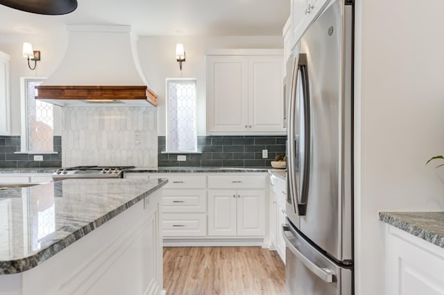 3621 121st St, Lubbock, TX 79423 - kitchen featuring freestanding refrigerator, premium range hood, white cabinetry, and backsplash