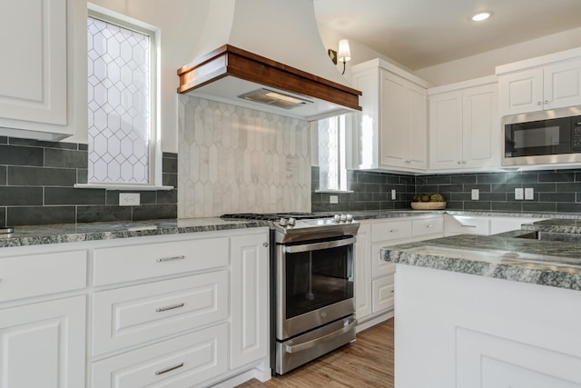 3621 121st St, Lubbock, TX 79423 - kitchen with appliances with stainless steel finishes, custom range hood, white cabinetry, light wood finished floors, and tasteful backsplash