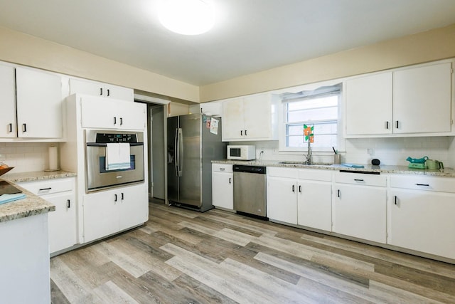 kitchen with sink, appliances with stainless steel finishes, white cabinetry, tasteful backsplash, and light wood-type flooring