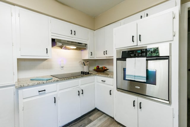 kitchen with oven, black electric stovetop, range hood, decorative backsplash, and white cabinets