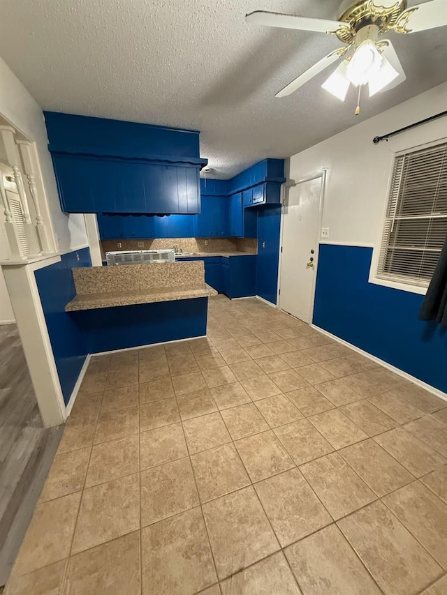 kitchen featuring ceiling fan, blue cabinets, kitchen peninsula, and light tile patterned floors