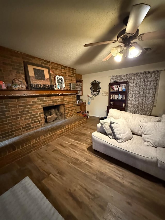 living room with ceiling fan, hardwood / wood-style floors, a brick fireplace, and a textured ceiling