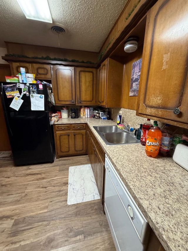 kitchen with dishwasher, sink, light wood-type flooring, black fridge, and a textured ceiling