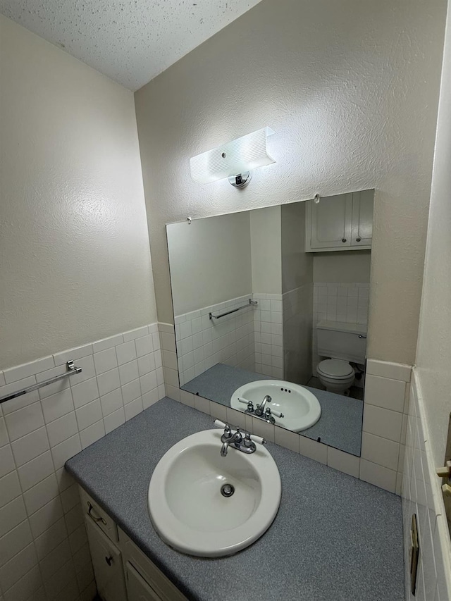 bathroom with vanity, tile walls, a textured ceiling, and toilet