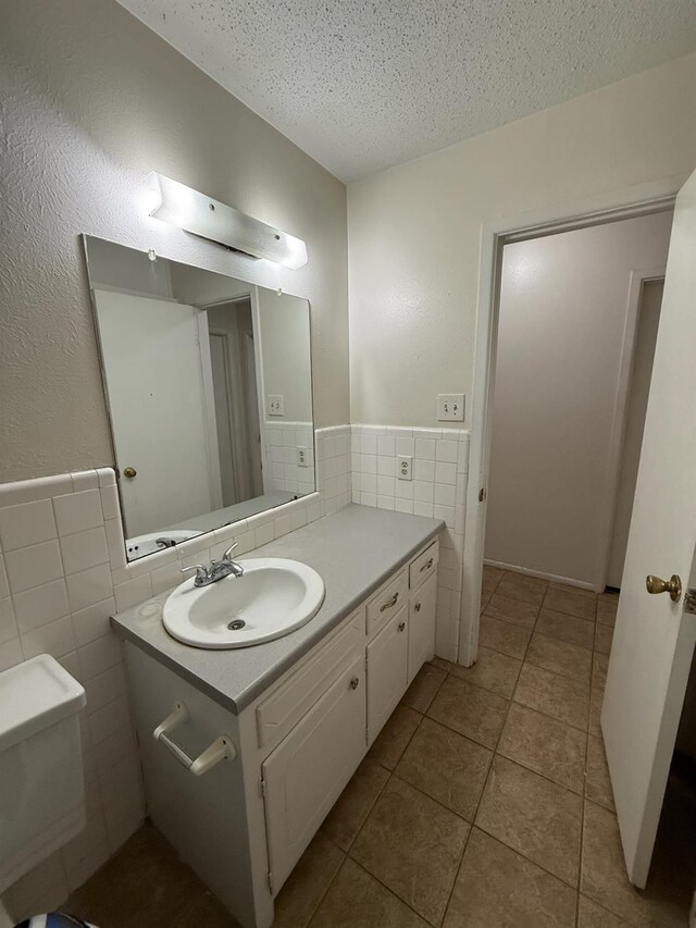 bathroom featuring tile walls, tile patterned flooring, vanity, toilet, and a textured ceiling