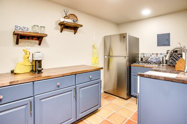 kitchen featuring butcher block countertops, backsplash, stainless steel fridge, light tile patterned floors, and electric panel