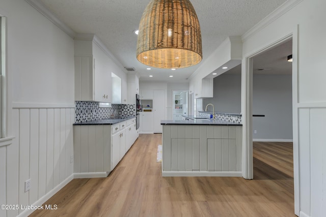 4013 48th St, Lubbock, TX 79413 - kitchen with dark countertops, light wood-type flooring, ornamental molding, decorative backsplash, and white cabinetry